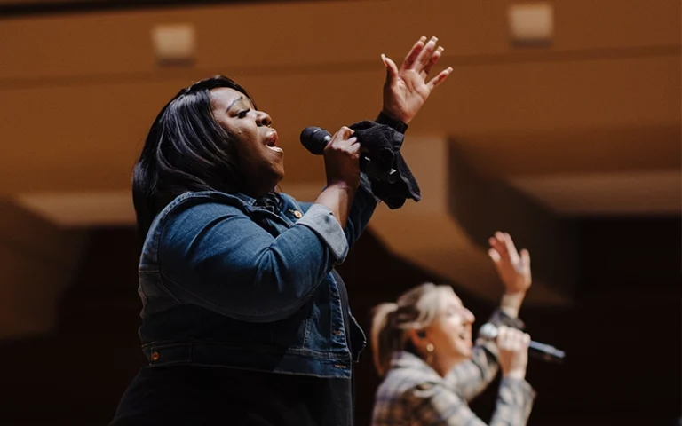 A worship leader holding a microphone and leading worship during the Palm Sunday service at New City Church in Naperville.